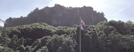 View of Guam mountain top with high cliffs, blue sky, and flags in the foreground